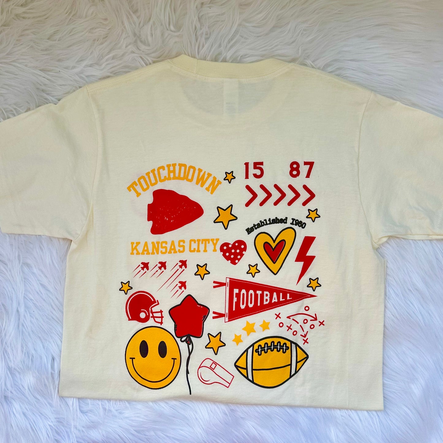 Beige t-shirt with colorful graphics and text on a white fur background