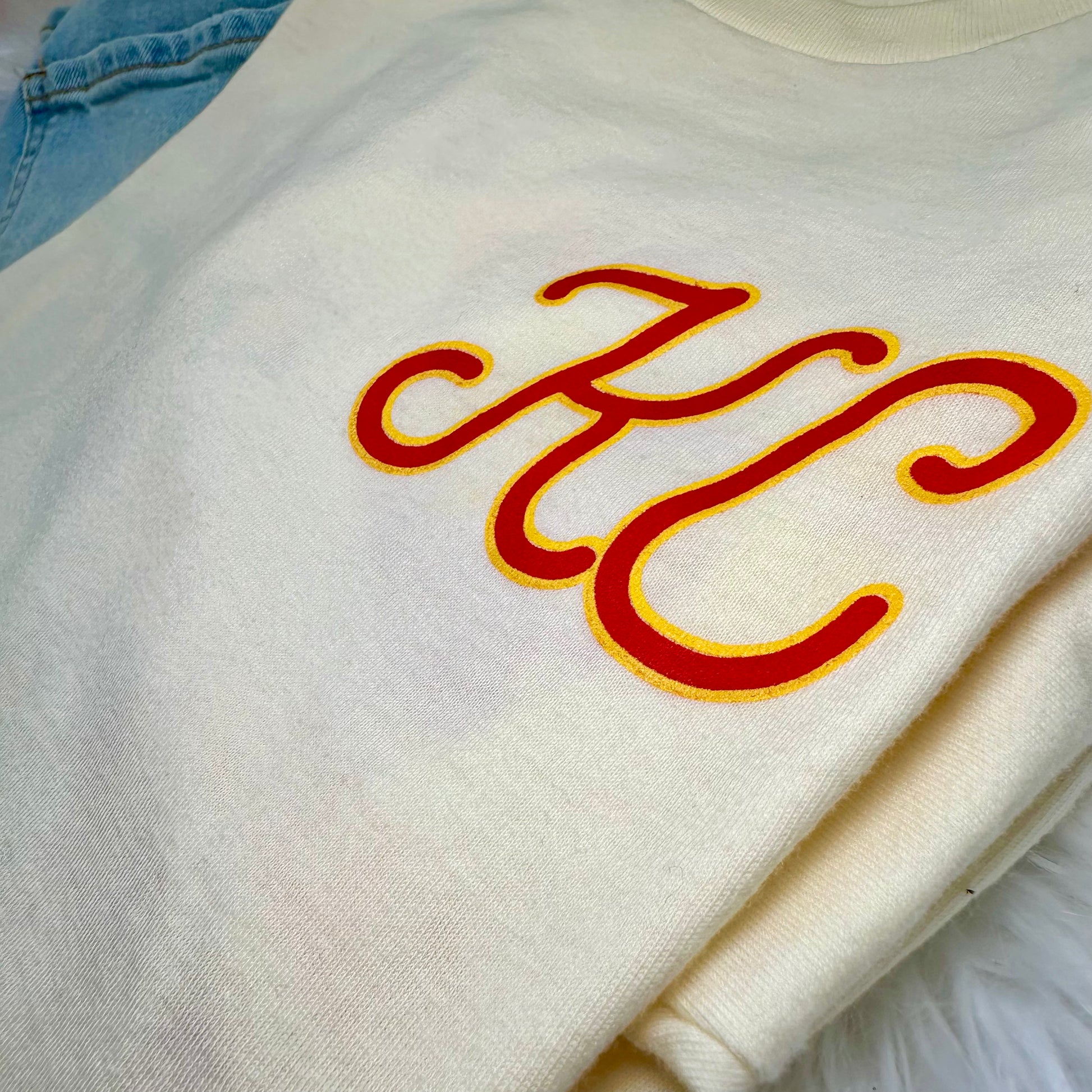 White tshirt with red and yellow 'KC' letters on a light blue background