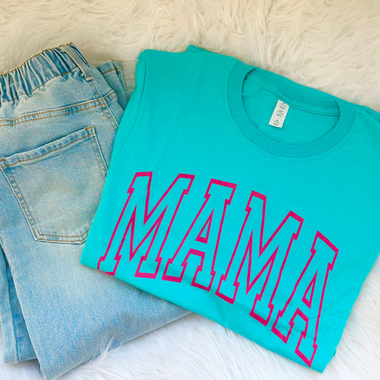 Turquoise t-shirt with 'MAMA' in pink on a white surface with jeans.