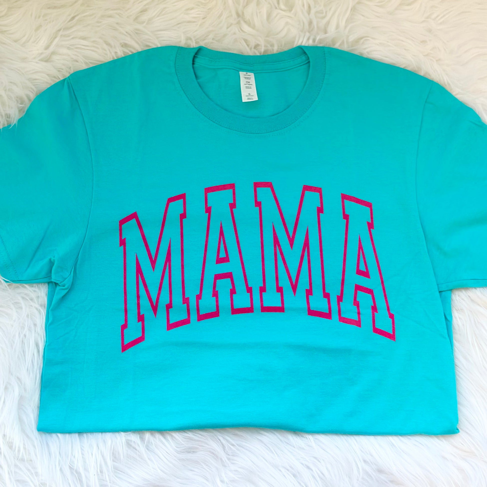 Turquoise t-shirt with 'MAMA' printed in pink on a white fluffy surface