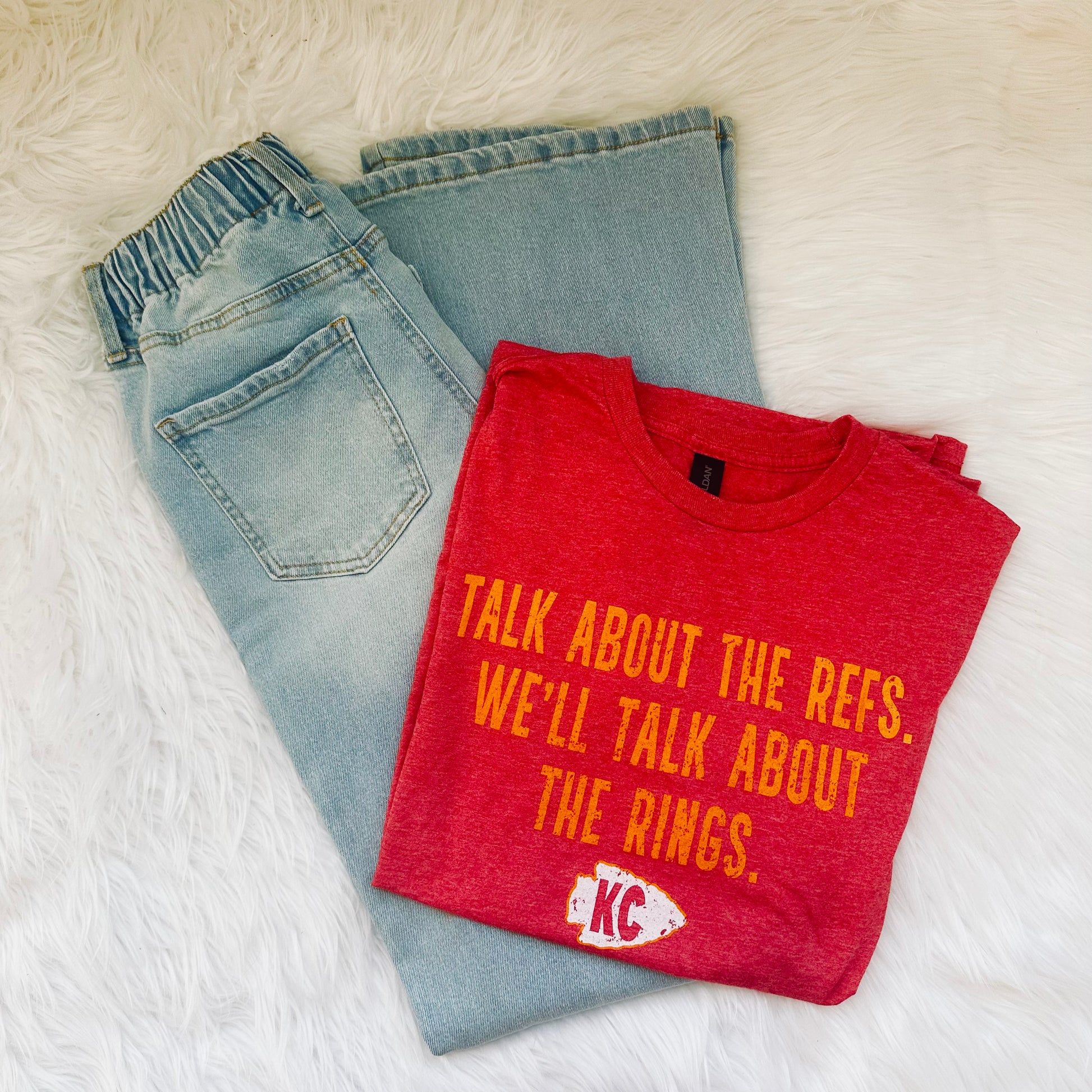 Folded red t-shirt with yellow text and a logo on a white surface with light blue jeans.