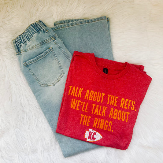 Folded red t-shirt with yellow text and a logo on a white surface with light blue jeans.